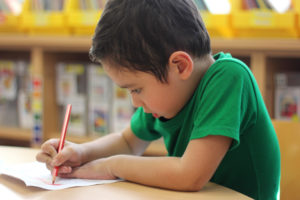 One boy bending over, intently writing on note paper