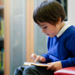Boy with royal blue sweater points at words while reading